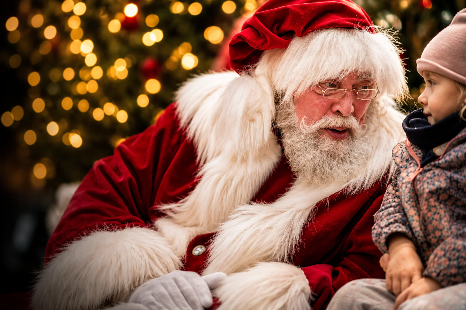Le Père Noël et un jeune enfant échangent un regard émerveillé, éclairés par des lumières de Noël chaudes