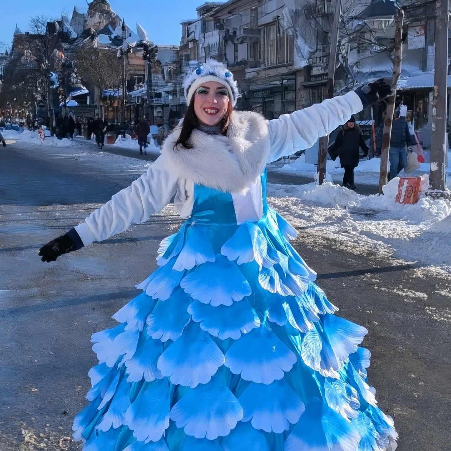 La Reine Flocon dans sa robe de pétales bleus, dans une rue enneigée.