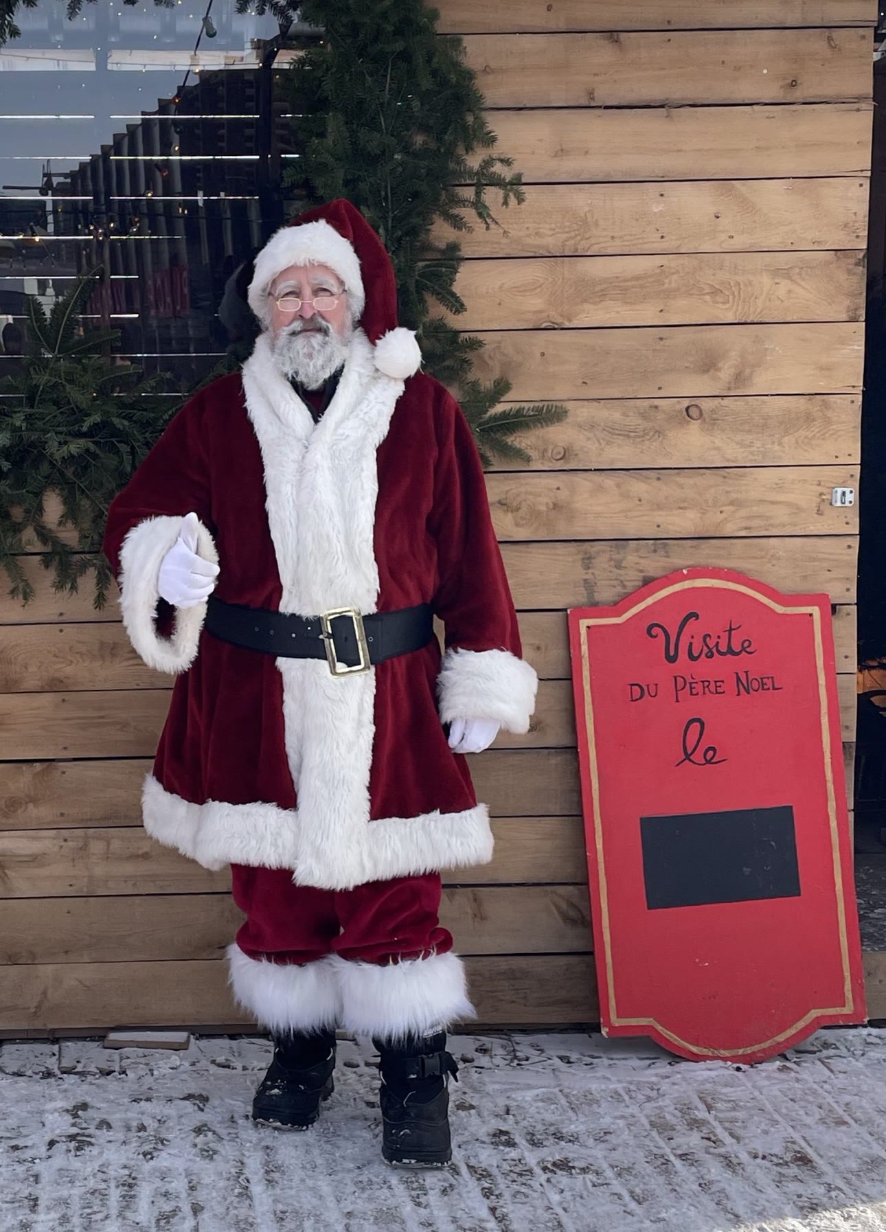 Le Père Noël Gilles devant un chalet de bois enneigé.