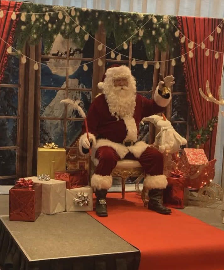 Le Père Noël Michel assis sur son trône devant un décor de fenêtre enneigée.