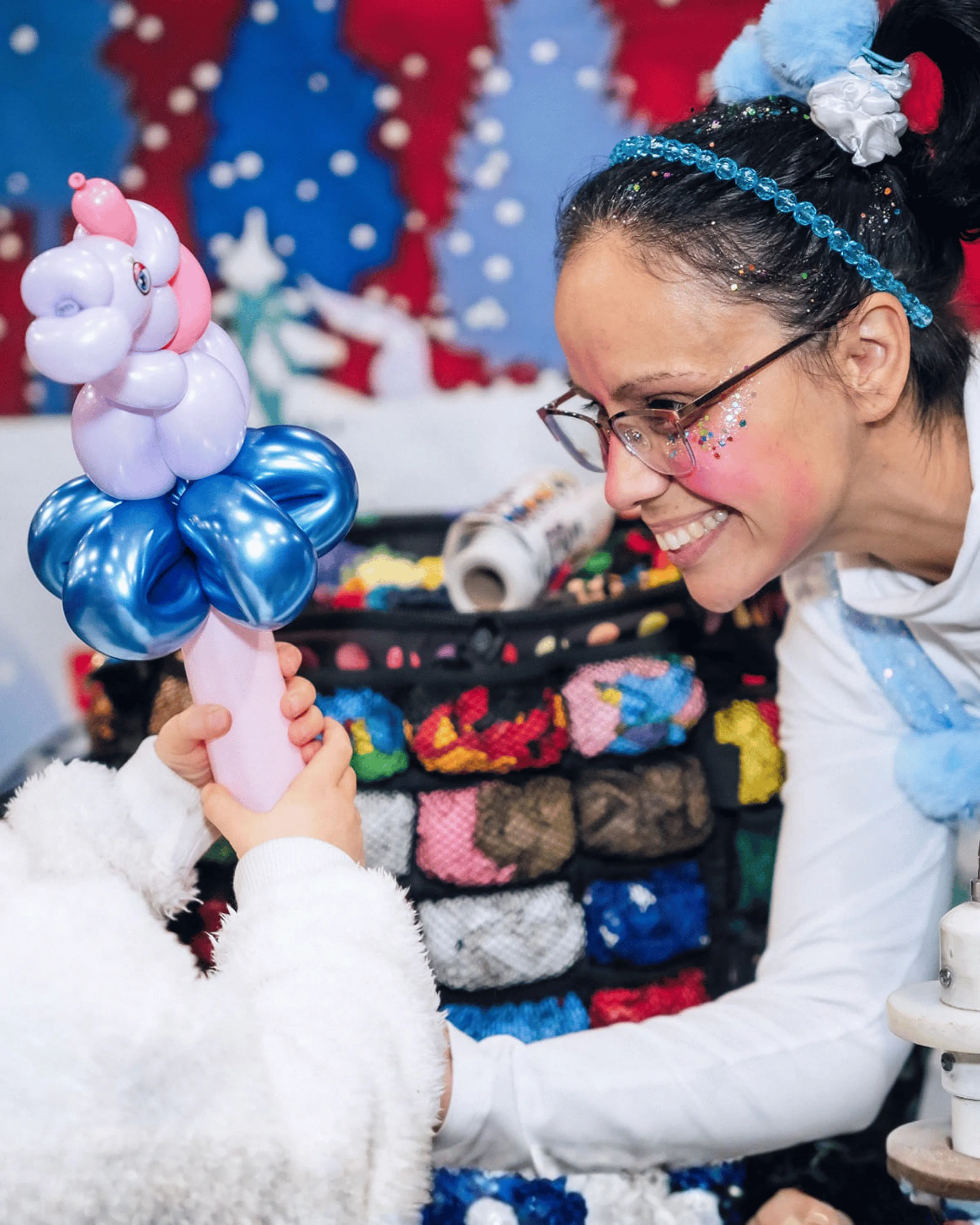 Une sculptrice de ballons présente ses créations devant une bannière de Noël.