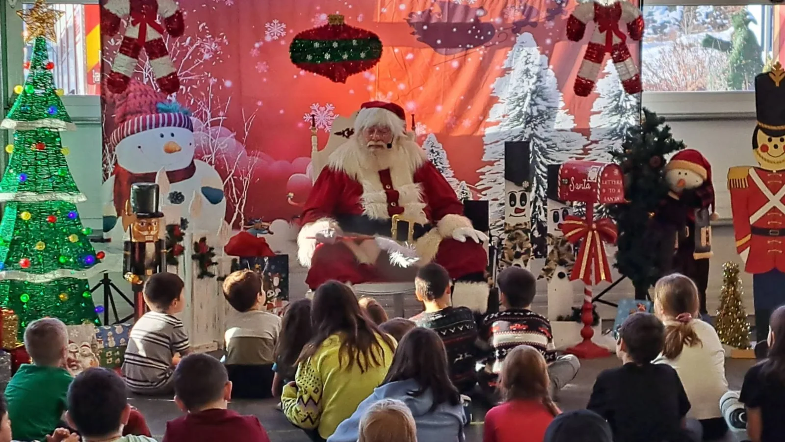 Le Père Noël assis devant un décor de Noël, entouré d'enfants assis par terre qui l'écoutent.