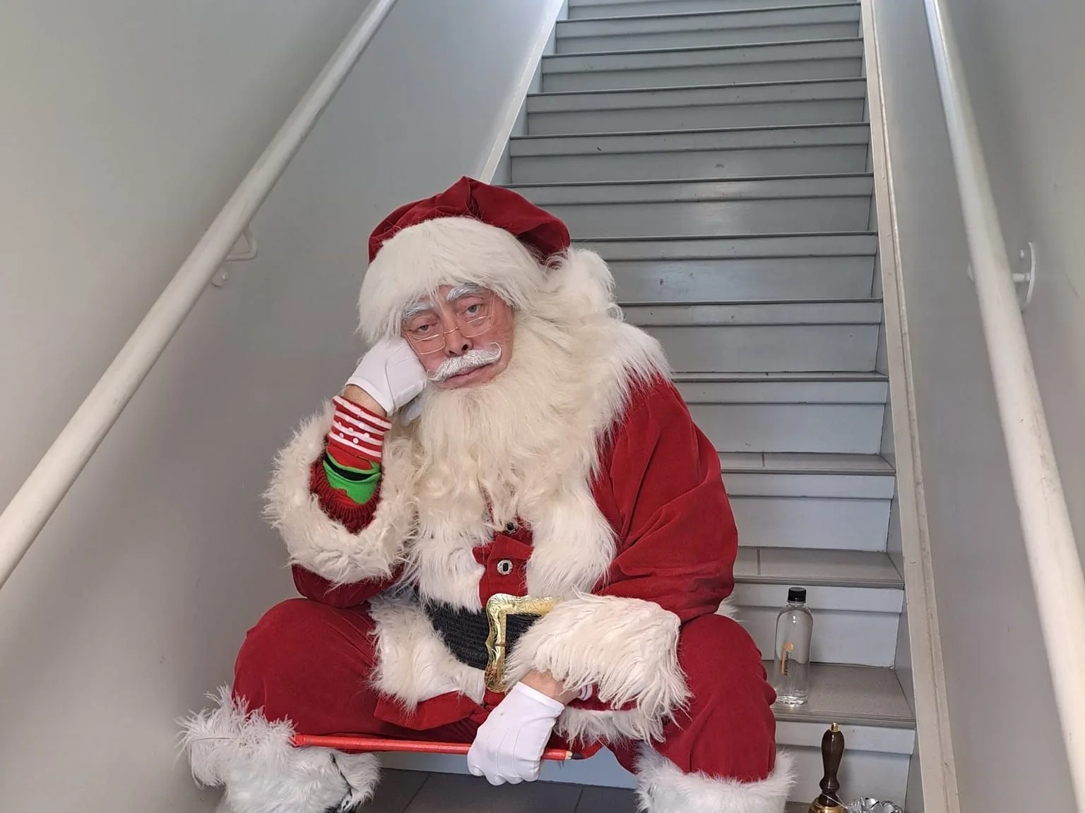 Le Père Noël assis dans un escalier, la tête appuyée sur la main, l'air épuisé.